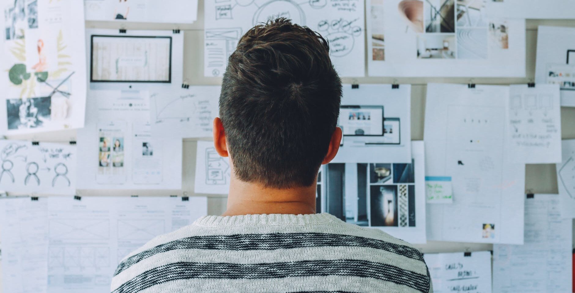 man wearing black and white stripe shirt looking at white printer papers on the wall