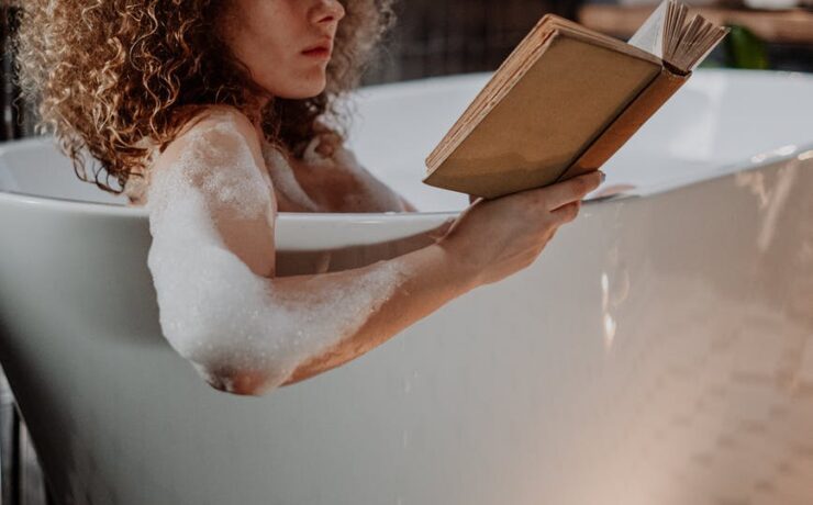 woman taking time for self care, reading a book and enjoying a bubble bath.